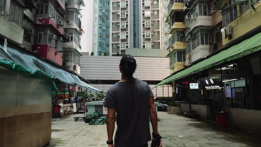 Man wearing a short sleeved shirt walks down a street that is lined with retail stores as a woman walks nearby carrying shopping bags