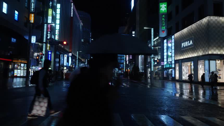 Silhouette of pedestrians carrying umbrellas walk on the intersection of a big city at night