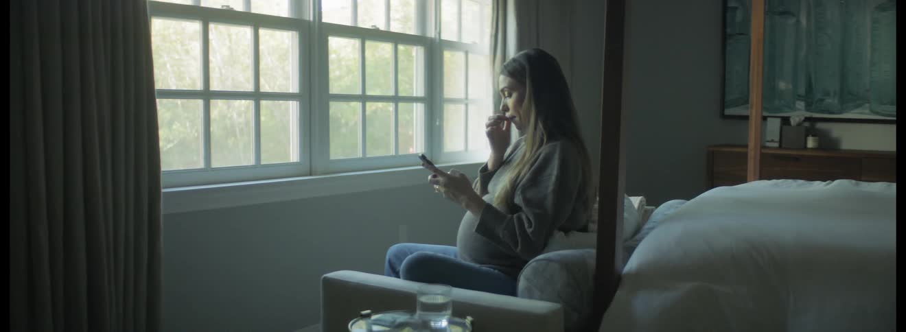 Young pregnant woman sitting on a couch in the bedroom at home checking her phone
