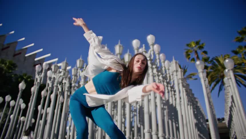 A female dancer performs a series of dance moves outside in front of numerous lamp posts