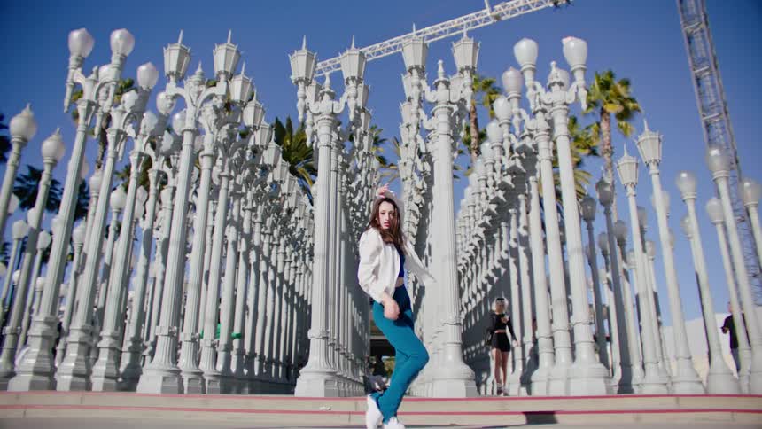 A woman dances in front of a public art display as people walk behind her