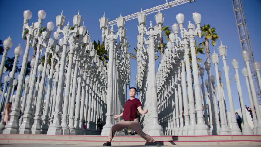 Young asian man energetically dancing in front of street lamps on a park in the city