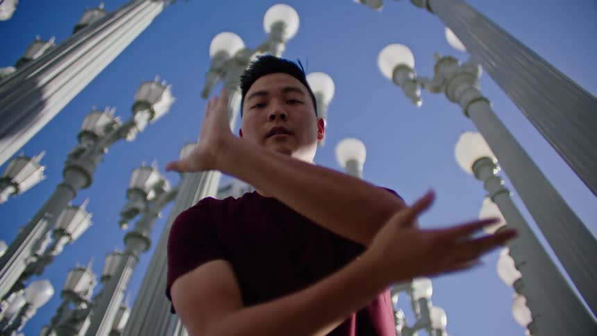 Man wearing a red shirt moves his arms as he dances near the light posts under a blue sky