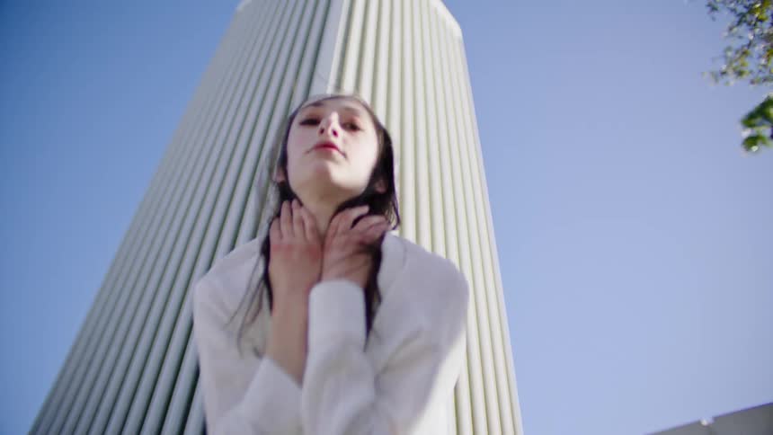 Woman in a blue top and white shirt dances in front of a skyscraper under a blue sky