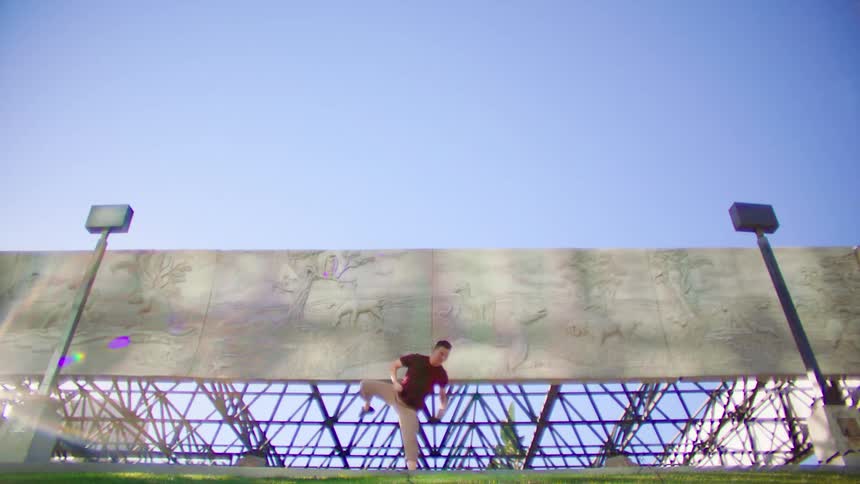 Young asian man energetically dancing in front of a metallic structure under a blue sky