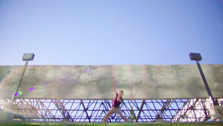 Man wearing a red shirt dances outdoors in front of cement murals on a sunny day