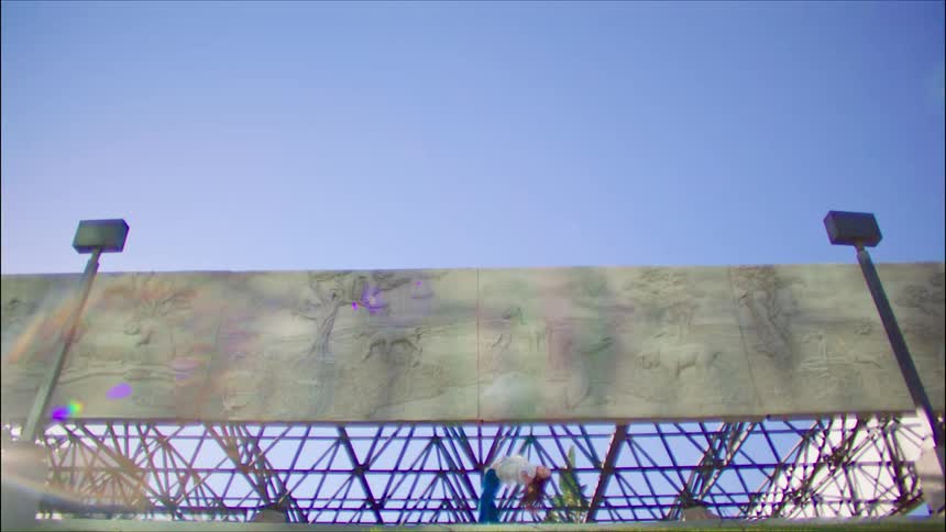 Young woman energetically dancing in front of a metallic structure under a blue sky