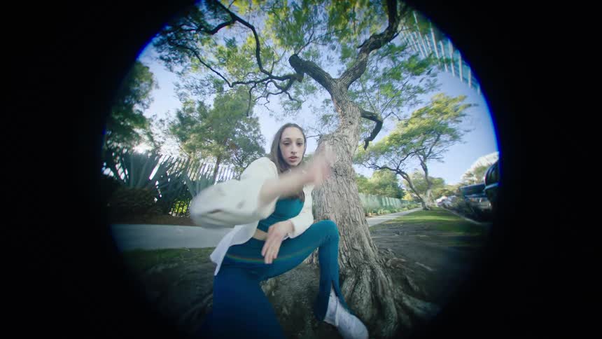 Female dancer with white shirt and teal top and pants dances next to tree on the sidewalk