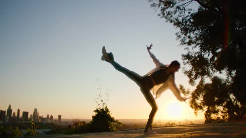 The silhouette of a female dancer is illuminated by sunlight as she kicks her leg high into the air
