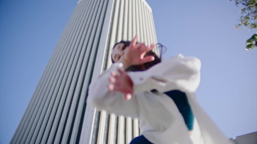 Young woman energetically dancing in front of a white skyscraper in the city