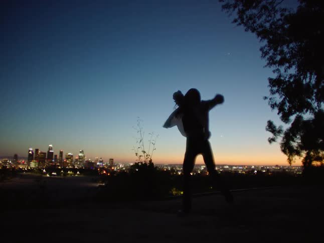 Dancing woman is silhouetted against the illuminated skyscrapers and sky at dusk