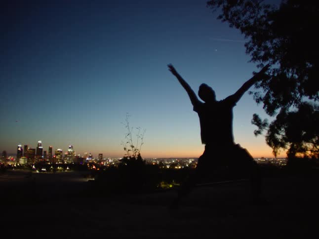 Dancing man is silhouetted against the illuminated skyscrapers and sky at dusk
