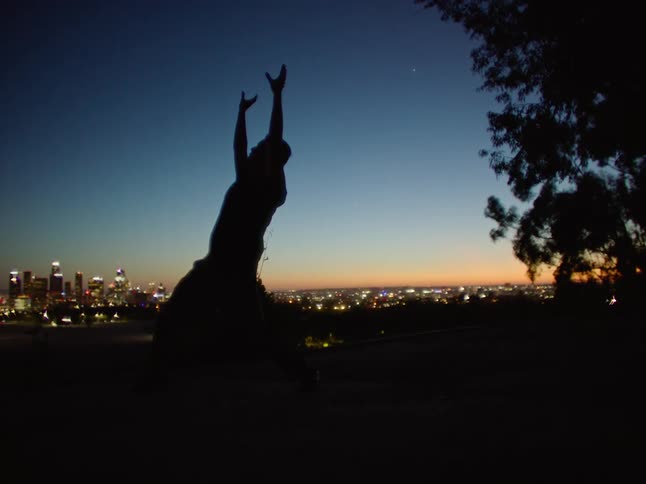 Dancing man is silhouetted against the illuminated skyscrapers and sky at dusk