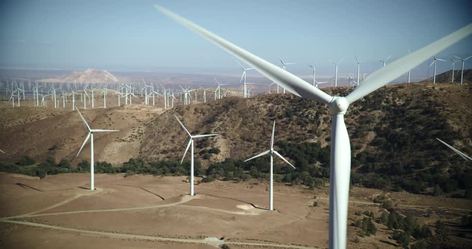 Wind turbines are spinning on a wind farm along the top of a mountain ridge under a clear sky
