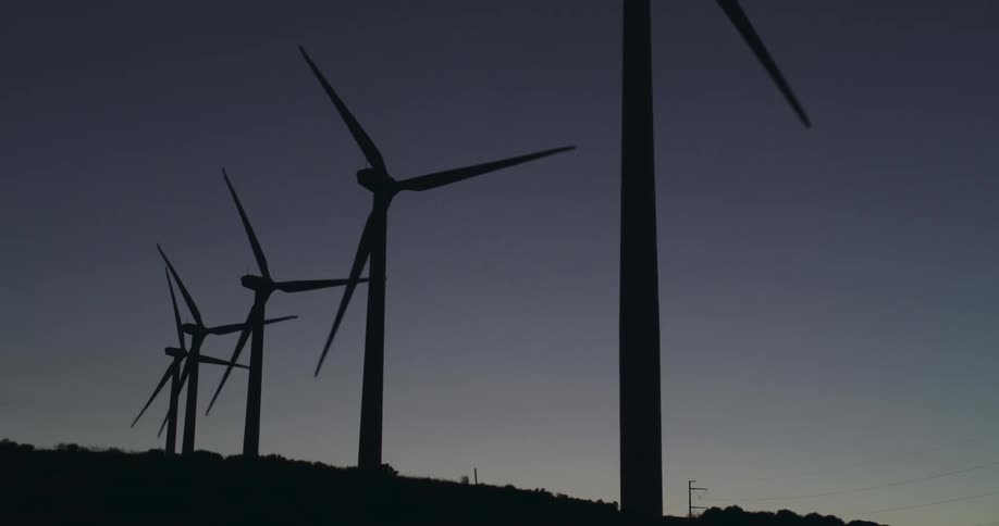 Wind turbines are silhouetted against the sky at dusk
