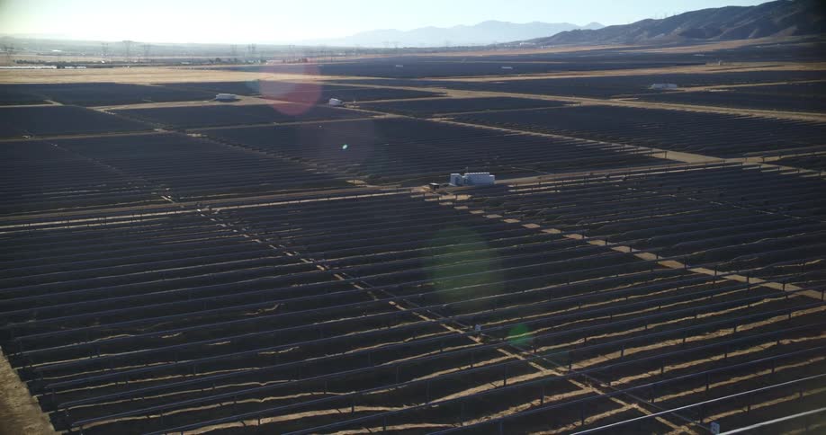 The sun shines brightly on solar panels on a solar farm with mountains in the distance