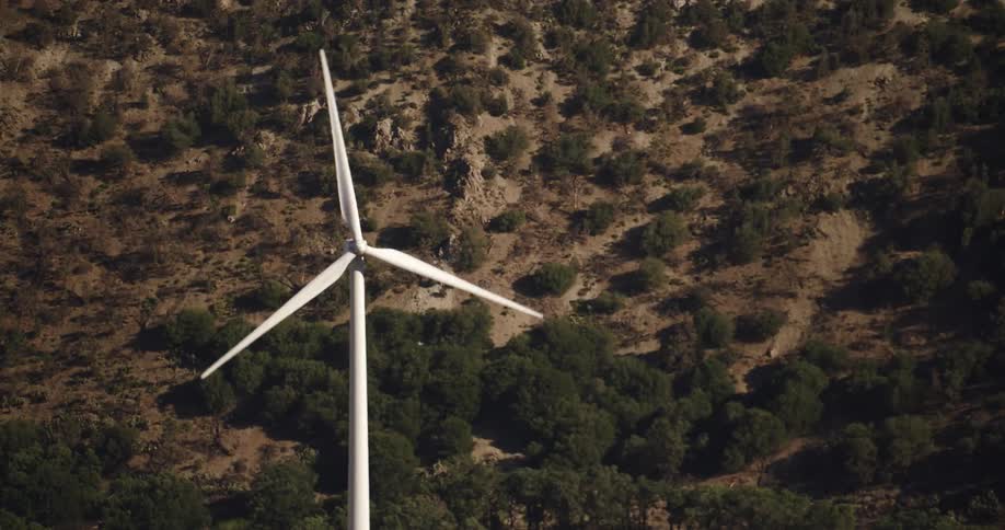 White spinning wind turbine comes into focus in front of a hill