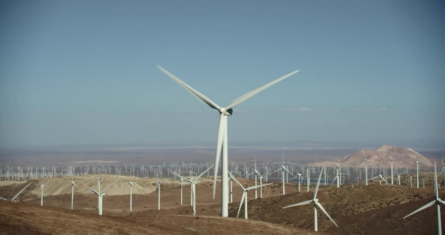 Many wind turbines are spinning on a wind farm under a clear sky with mountains in the distance