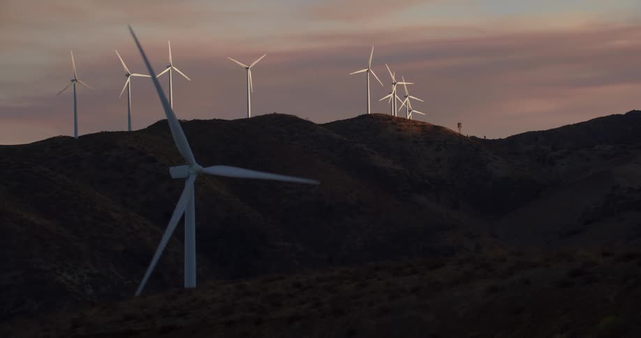 Wind turbines run on wind farm in the hills at dusk