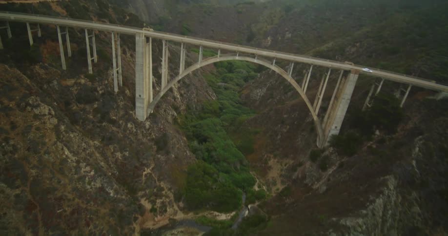 A bridge over a ravine near where rough water waves are rolling in on the beach as they crash into rocks along the shore