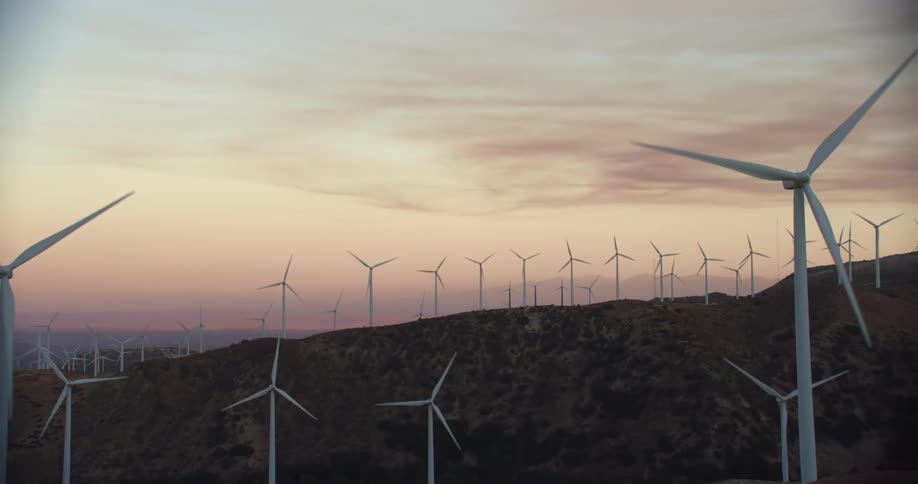 Wind turbines run on wind farm in the hills at dusk