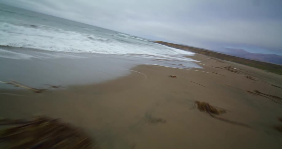 Ocean waves curls and splash to shore while birds fly above on a cloudy day