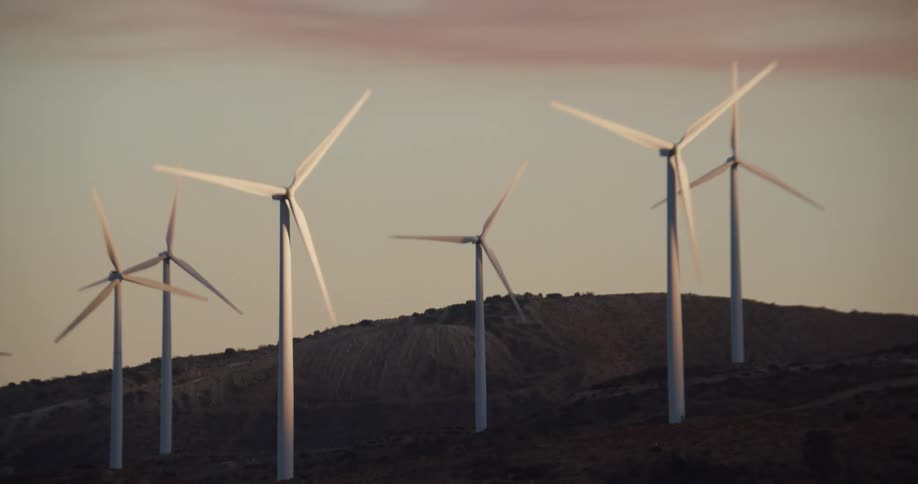 Wind turbines are spinning on a wind farm with mountains in the distance