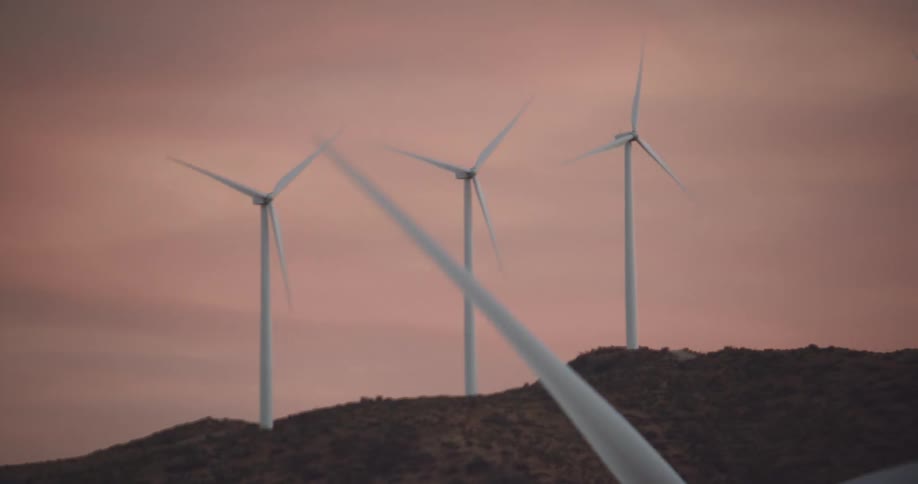 Wind turbines spin on a hill in front of a pink sky