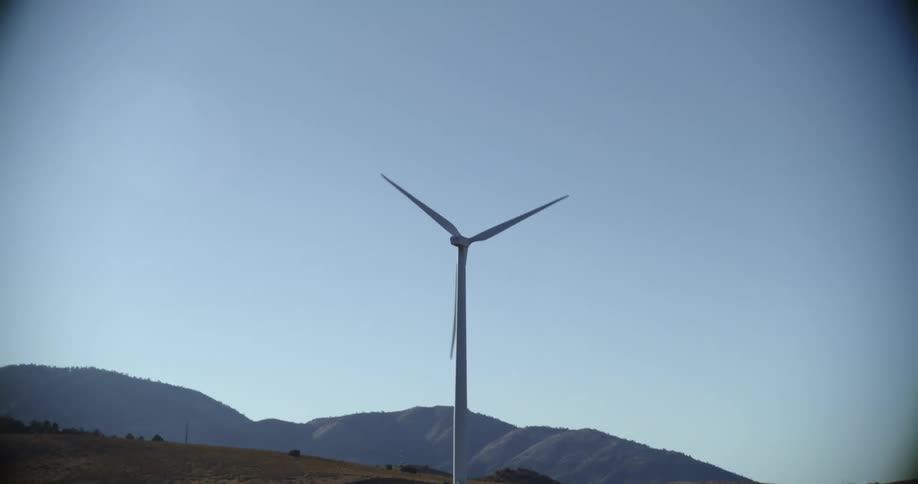 Wind turbine spinning in a field near the hills under a blue sky