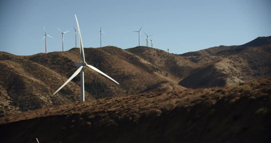 Wind turbines are spinning on a wind farm along hilltops under a clear sky