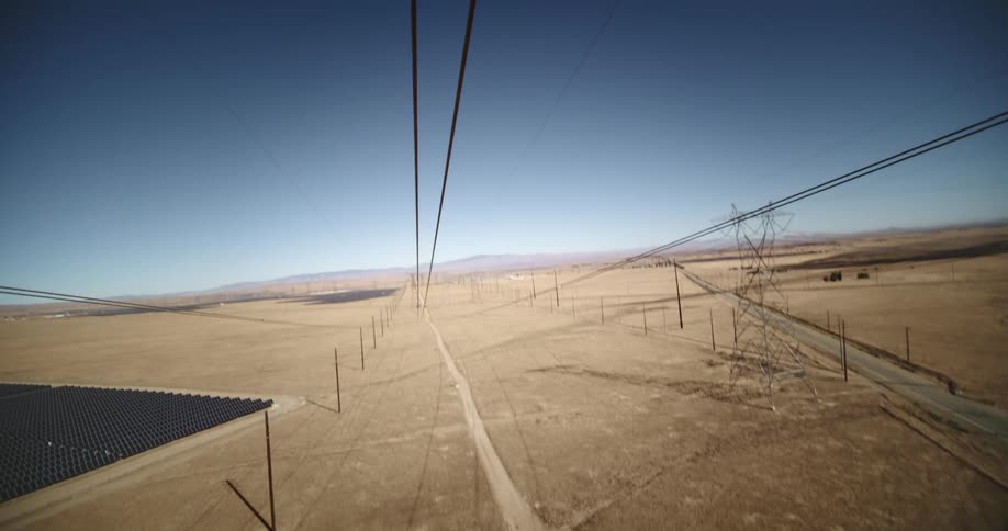 Utility towers and power lines are in open desert land with mountains on the horizon under a clear sky