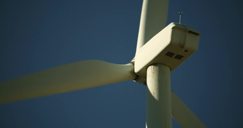 White blades on a wind turbine spinning in front of a clear deep blue sky