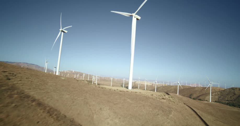 Many wind turbines are spinning on a wind farm under a clear sky with mountains in the distance