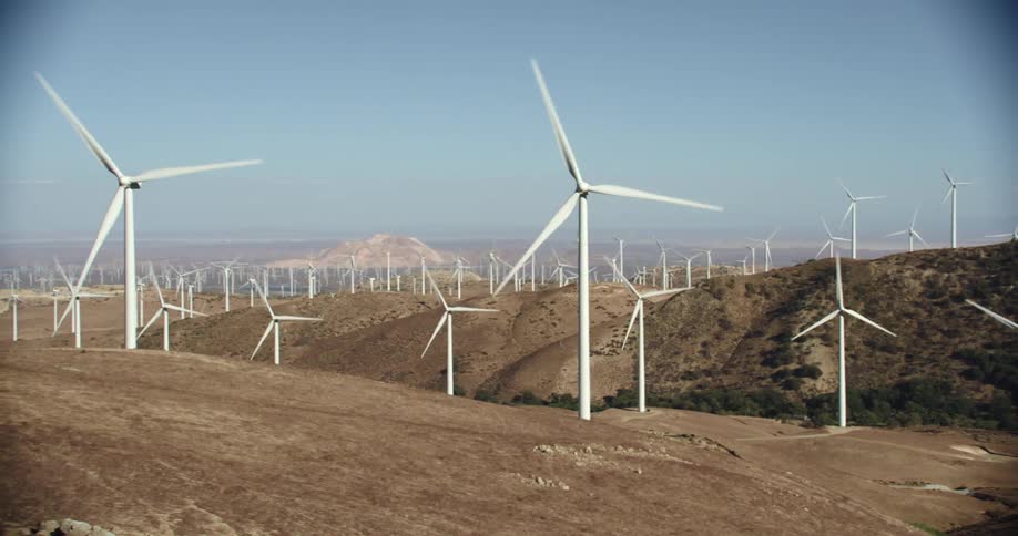 Many wind turbines are spinning on a wind farm under a clear sky with mountains in the distance