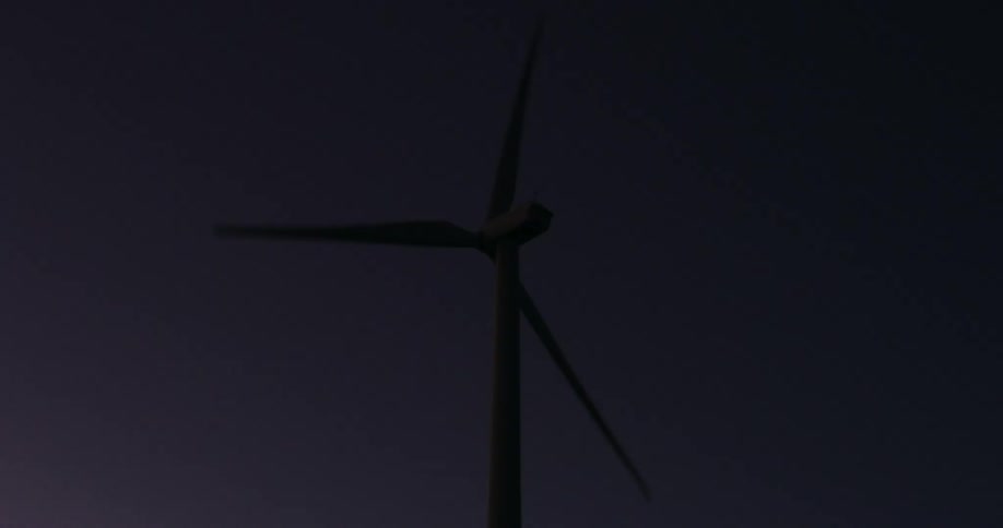 A wind turbine spins in a darkening sky