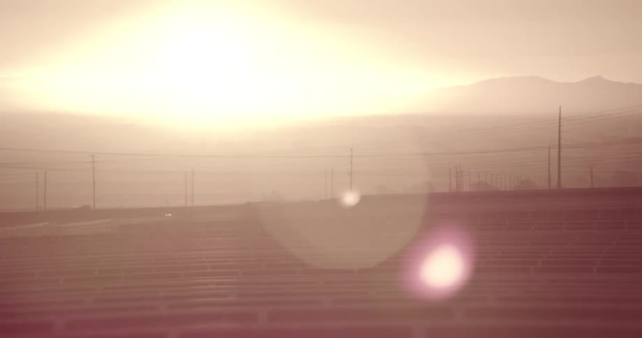 Rows of solar panels in front of tall transmission towers in the desert at sunset