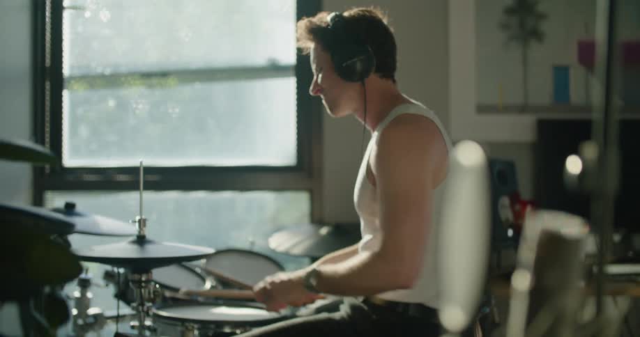 The camera pulls away from a man playing drums in home studio