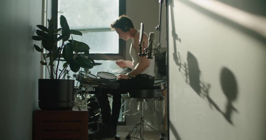 A man wears headphones while playing the drums at home