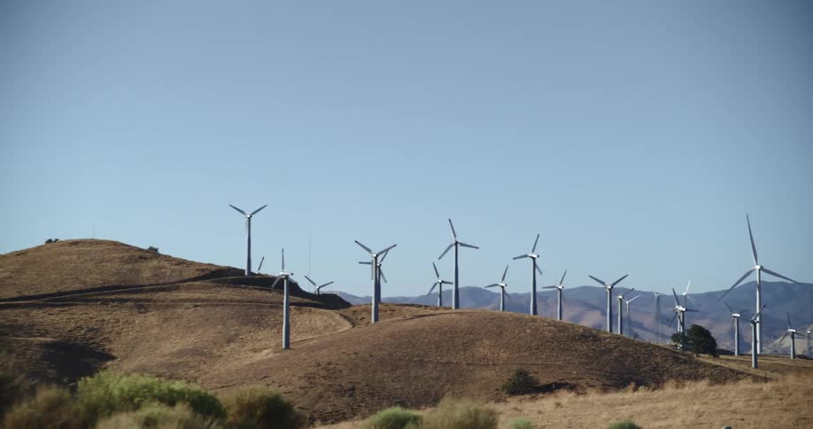 Wind turbines are spinning on a wind farm along hills with mountains in the distance