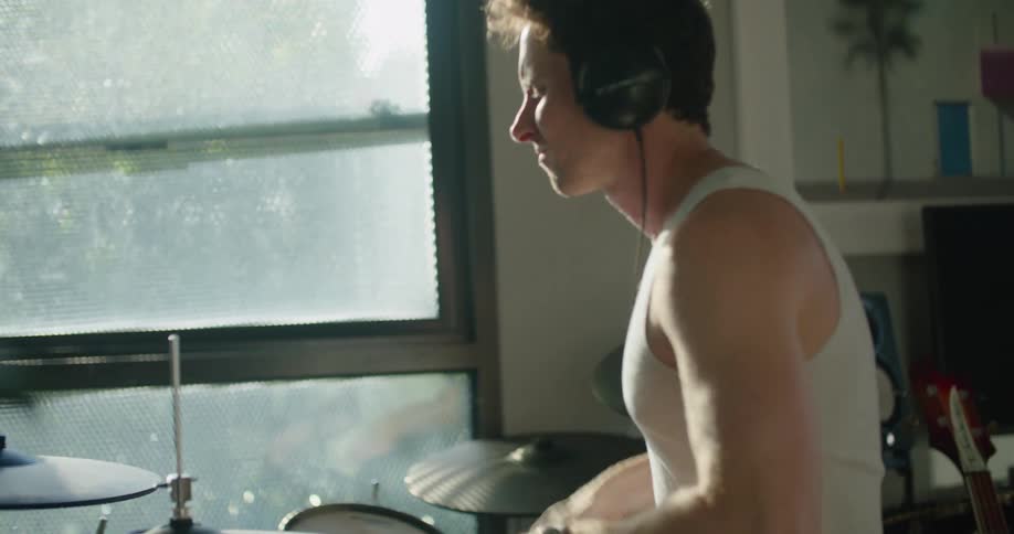 Man wearing headphones playing drums indoors next to a glass window
