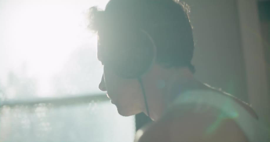 Young man wearing headphones playing drums in the living room at home in the morning