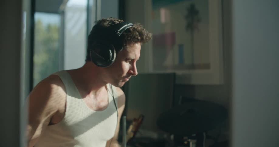 Man wearing headphones playing drums indoors in front of a mirror