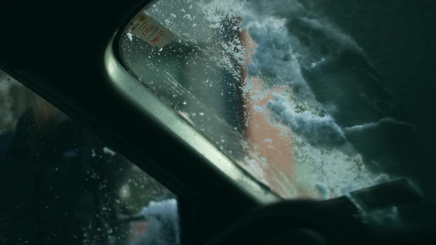Interior view from car of women scraping snow off the windshield