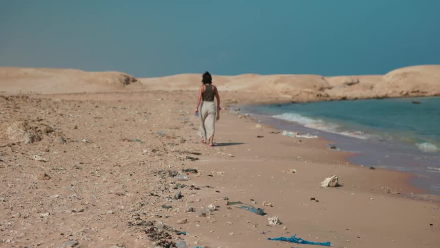 A woman walks across a rocky beach under a clear sky