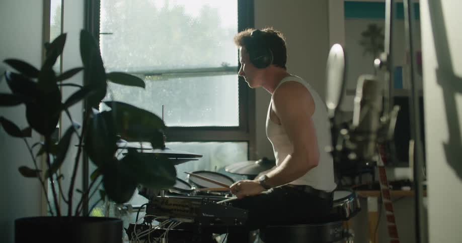 Young man wearing headphones playing drums in the living room at home in the morning