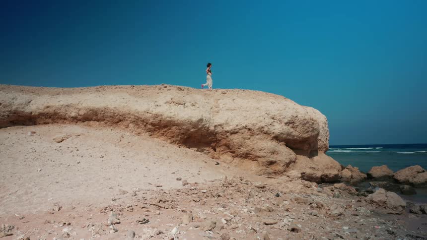 Woman running over the rocks near the coast close to the ocean