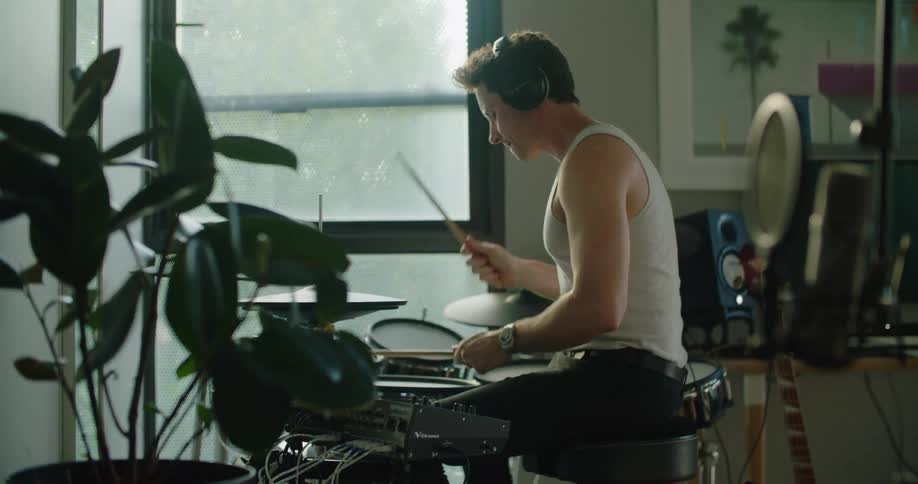 Man wearing headphones playing drums indoors near a glass window