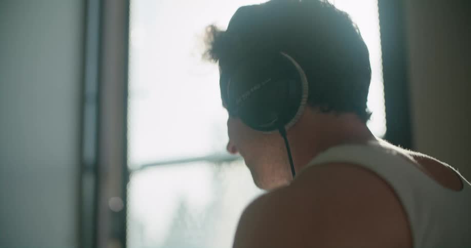 Young man wearing headphones playing drums in the living room at home in the morning