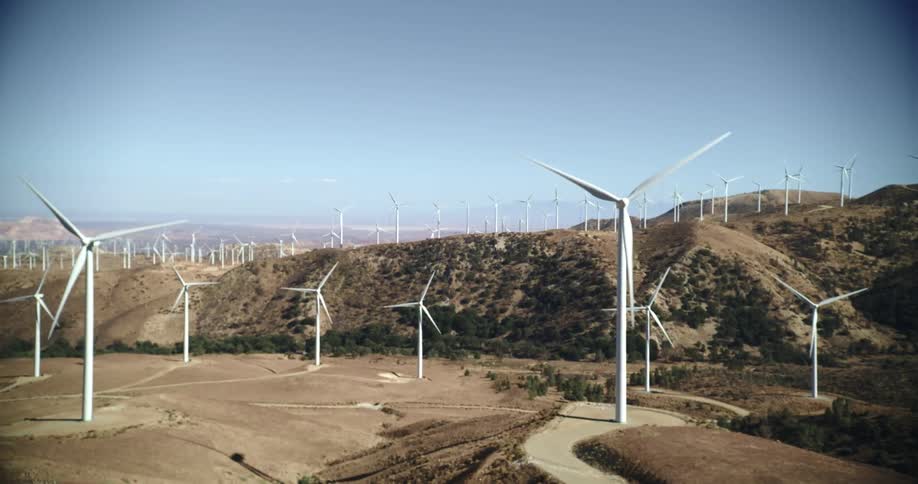 Wind turbines are spinning on a wind farm along the top of a mountain ridge under a clear sky