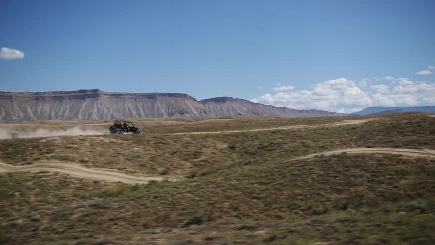 Four people riding a quad all terrain buggy vehicle kicking dust on a dirt road in the badlands